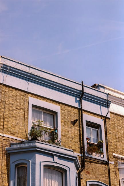 Exterior view of a converted Victorian house with a brick facade and white decorative trim, under a clear blue sky. The building features two windows with white frames and flower boxes, and the roof s